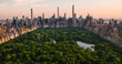 Aerial Helicopter Photo Over Central Park with Nature, Trees, People Having Picnic and Resting on a Field Around Manhattan Skyscrapers Cityscape. Beautiful Evening with Warm Sunset Light