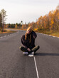 Eine Frau sitzt auf einer Straße in Norwegen mit Blick auf die herbstliche Landschaft Skandinaviens.