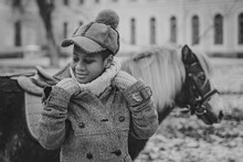 Boy Adjusting His Coat Collar Cutely Smiling Against The Background Of A Pony In Black And White