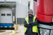 © Halfpoint - Truck driver standing with arms crossed leaning on red truck and looking at camera.