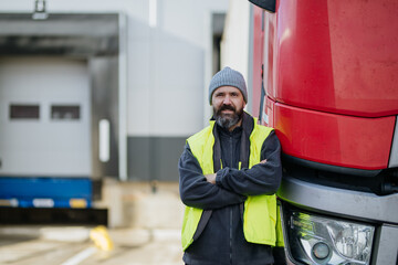 Truck driver standing with arms crossed leaning on red truck and looking at camera.