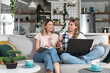 Two young women sitting on the sofa using laptop computer and credit card for online shopping and ordering groceries and food for home so they dont have to go out to buy food