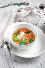 Wall Mural - Chicken broth with vegetables and herbs in a white bowl. Transparent soup with homemade chicken.