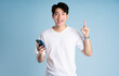 © STOCK88PHOTOGRAPHER - Portrait of Asian guy using phone and posing on blue background