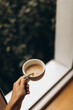 © Julia - with an outstretched hand in which a female fragile hand holds a cup of coffee with fragrant beautiful foam with a view of the green background of nature