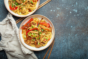 Poster - Two bowls with Chow Mein or Lo Mein, traditional Chinese stir fry noodles with meat and vegetables, served with chopsticks top view on rustic blue concrete background, space for text.