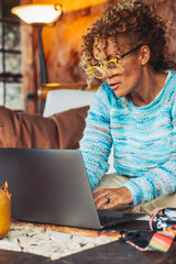 Modern cute woman adult middle age working at home with laptop computer sitting on the couch - technology online people lifestyle concept - adult female in smart working or digital job leisure