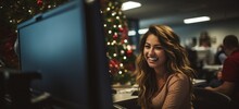 Office Holiday Spirit As Woman Works At Computer With Christmas Tree Backdrop. Seasonal Workplace.