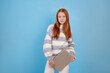 © Ирина Щукина - Confident redhead teenage girl holding laptop on blue background in studio.