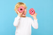 Boy with blond hair and freckles having fun with glazed donuts, sticking tongue out. Children and sugary junk food concept. Boy holding colorful donuts, eating junk unhealthy food full of sugar