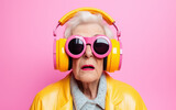 Fototapeta  - A funky stylish dressed elderly woman with sunglasses and headphones on pink background.