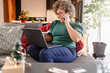 © lordn - A beautiful middle-aged woman doing holiday shopping from home browsing the internet on a computer and ordering by phone