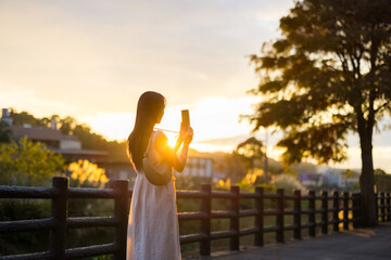 Poster - Woman use of mobile phone to take photo under sunset