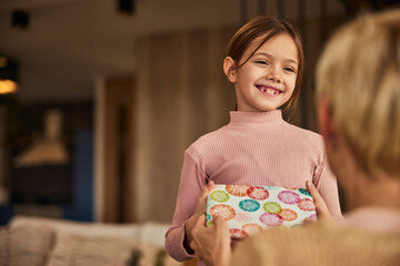 Wall Mural - A smiling grandchild giving a present to her grandma, looking happy.