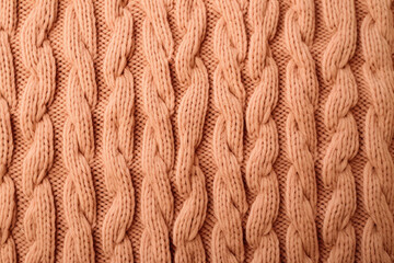A close up of a peach fuzz  knitted sweater with a large braid suitable for winter fashion websites, knitting blogs, cozy apparel advertisements, and seasonal social media posts.