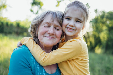 Little girl hugging smiling middle aged woman. Cute female kid and her grandmother enjoy walking outdoors