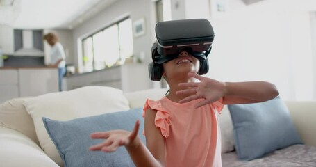 Wall Mural - happy biracial girl wearing vr headset using virtual interface in living room, slow motion
