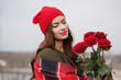 A young woman in a red hat and blanket with a bouquet of red roses