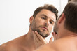 sexy man with stubble looks at the wrinkles on his face. Close up man looking in mirror, sensitive skin, cosmetology treatment. Skin care. joyful, virile, manly, attractive, naked, unshaven, handsome