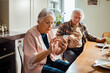 © Marko Geber - Senior woman using smartphone during breakfast with husband