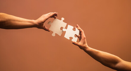 Wall Mural - Two hands trying to connect couple puzzle piece on gray background. Teamwork concept. Closeup hand of connecting jigsaw puzzle