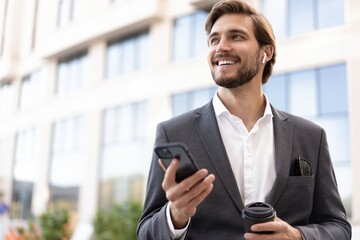 Wall Mural - Confident young businessman using cell phone and drinking coffee in the city.