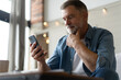 © opolja - Happy smiling senior man using smartphone device while sitting on sofa at home