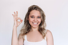 A Young Caucasian Attractive Blonde Woman With Wavy Hair Showing Okay Gesture With Her Hand Isolated On A White Background. Positive Human Emotion. The OK Approval Sign