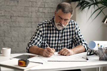 Sticker - Mature confident smiling architect in casual wear working with blueprint papers and drawings in modern lightful office.