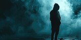 Fototapeta  - Silhouette of a man wearing a hoodie standing in a dark background