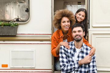 Portrait of happy family of tree with parents and small daughter traveling together by trailer motor home van home on wheels, caravanning looking at camera