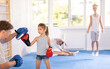 Young girl with her trainer father at gym. Boy wearing boxing gloves exercise and punch to pads for boxing