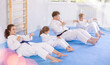 Concentrated tweens with parents in traditional martial arts attire participating in intense training session, practicing abdominal crunches combined with hand strikes