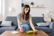 Front view of millennial woman holding eco-friendly silicone menstrual cup while reading use instructions sitting on sofa at home. Feminine hygiene lifestyle concept