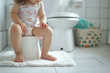 Child's legs hanging down from a potty in a bathroom. Training a toddler to use a toilet. Potty training, hygiene, childhood milestones.