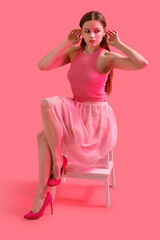 Wall Mural - Fashionable young woman sitting on chair against pink background