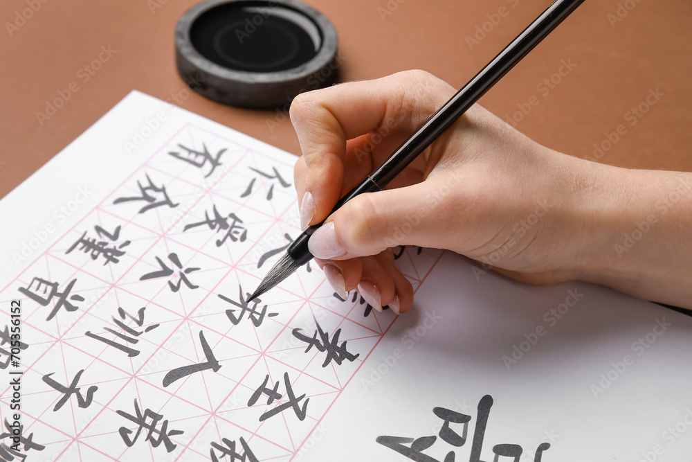 Woman writing Asian hieroglyphs on color background, closeup. International Haiku Poetry Day