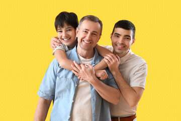 Wall Mural - Happy little boy with his dad and grandfather hugging on yellow background