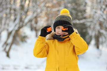 Sticker - Cute little boy covering eye with tangerine in snowy park on winter day