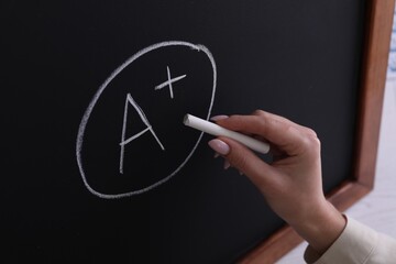 Wall Mural - School grade. Teacher writing letter A and plus symbol with chalk on blackboard, closeup