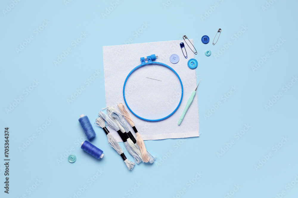 Plastic embroidery hoop with canvas and sewing supplies on blue background