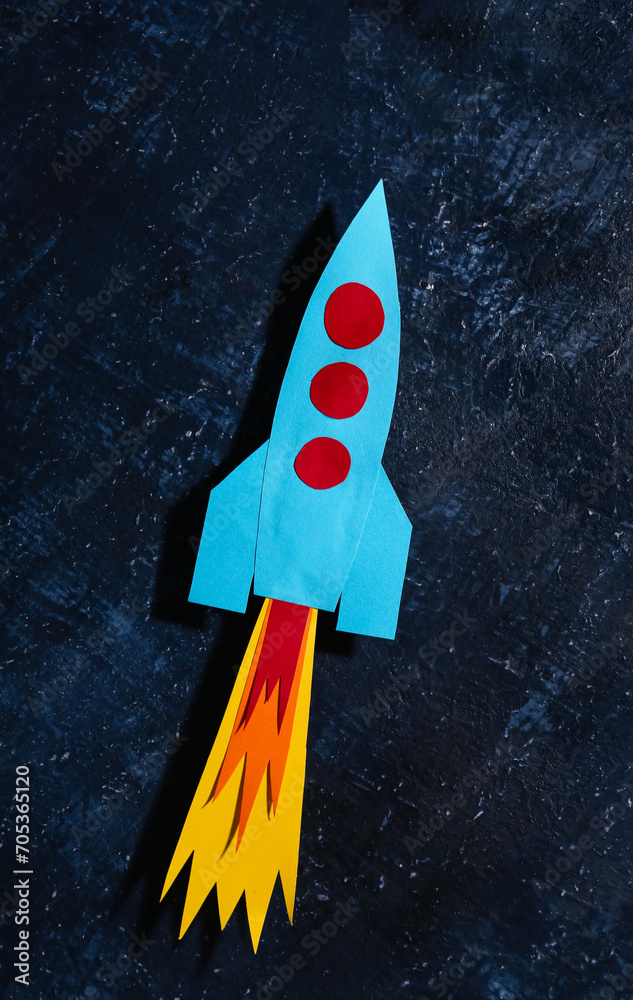 Blue paper rocket on dark grunge background