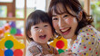 日本の幼稚園児と先生/親子がカラフルなおもちゃで笑顔で遊んでいる写真、背景保育ルーム、木育/幼児教育
