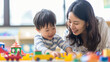 日本の幼稚園児と先生/親子がカラフルな木製のおもちゃで笑顔で遊んでいる写真、背景保育ルーム、木育/幼児教育