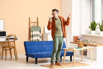 Wall Mural - Angry young man talking by mobile phone in living room