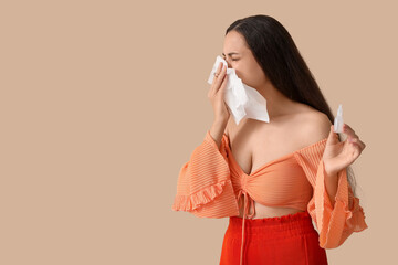 Wall Mural - Allergic young woman with nasal drops and tissue on beige background