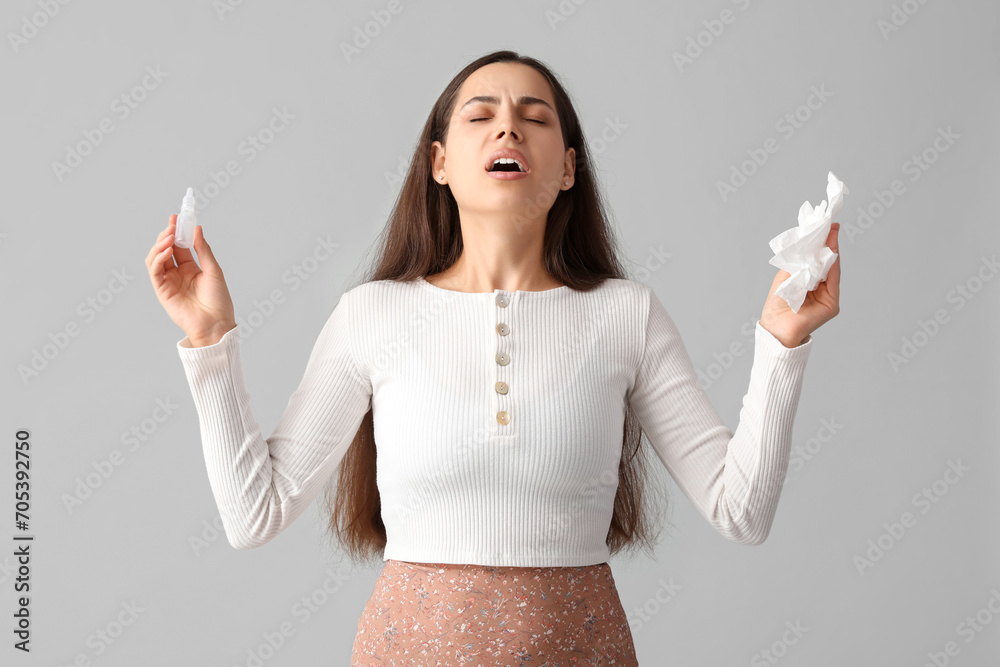 Allergic young woman with nasal drops and tissue on grey background