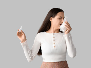 Canvas Print - Allergic young woman with nasal drops and tissue on grey background