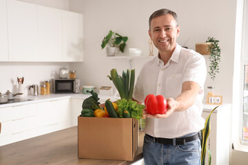 Wall Mural - Mature man with cardboard box of fresh vegetables at table in kitchen