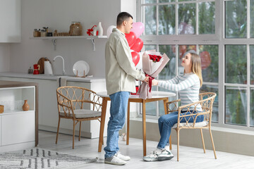 Poster - Beautiful young couple with bouquet of roses celebrating Valentine's Day in kitchen at home